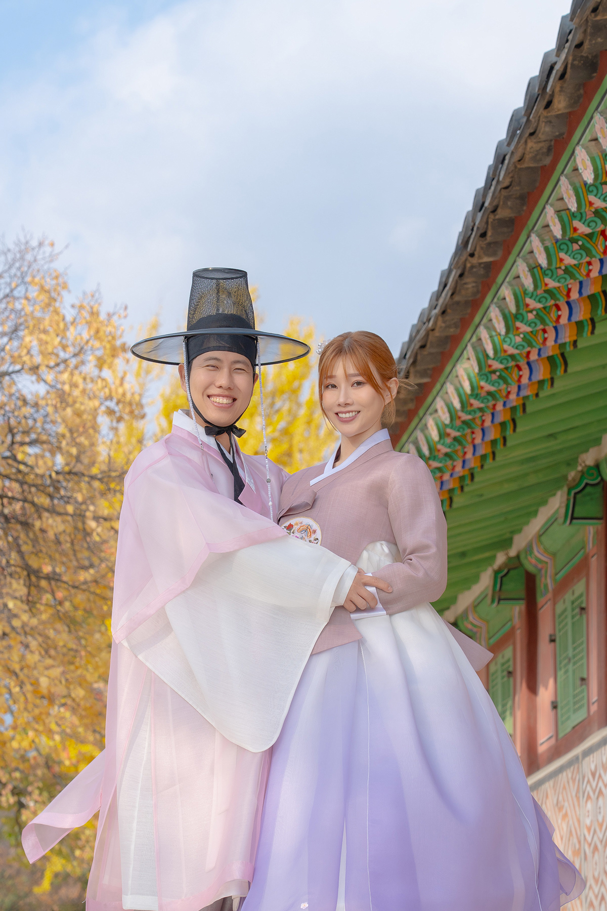 A smiling couple wearing pastel hanbok at a Seoul palace in autumn