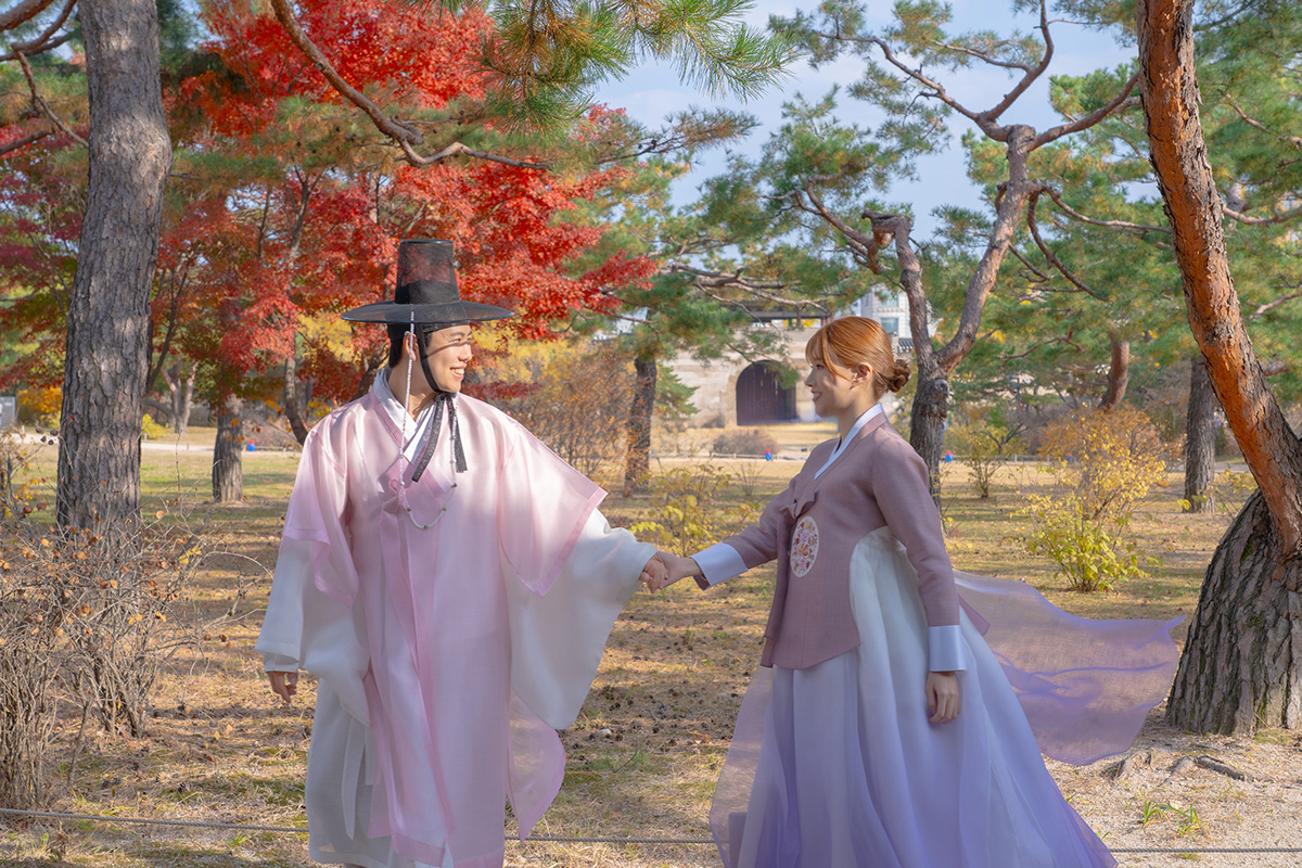 A couple walking hand in hand among autumn trees in hanbok