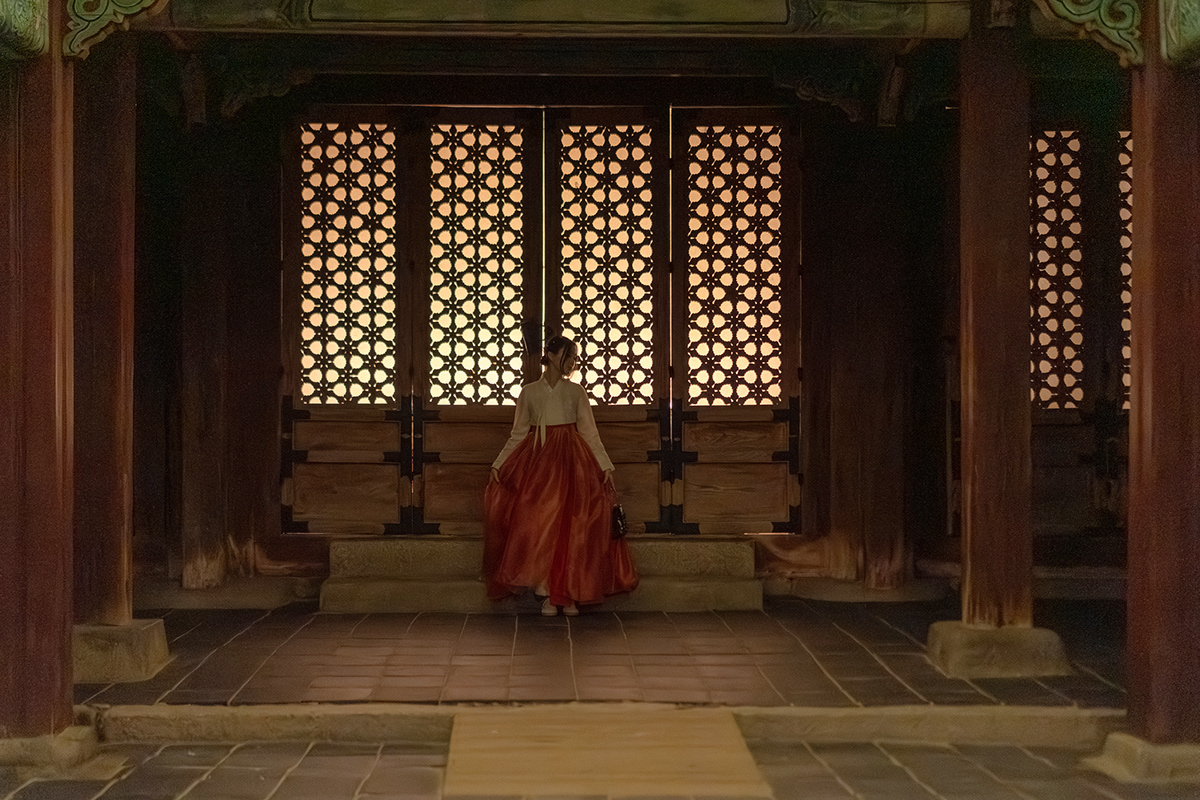 A solo hanbok portrait framed by traditional palace doors