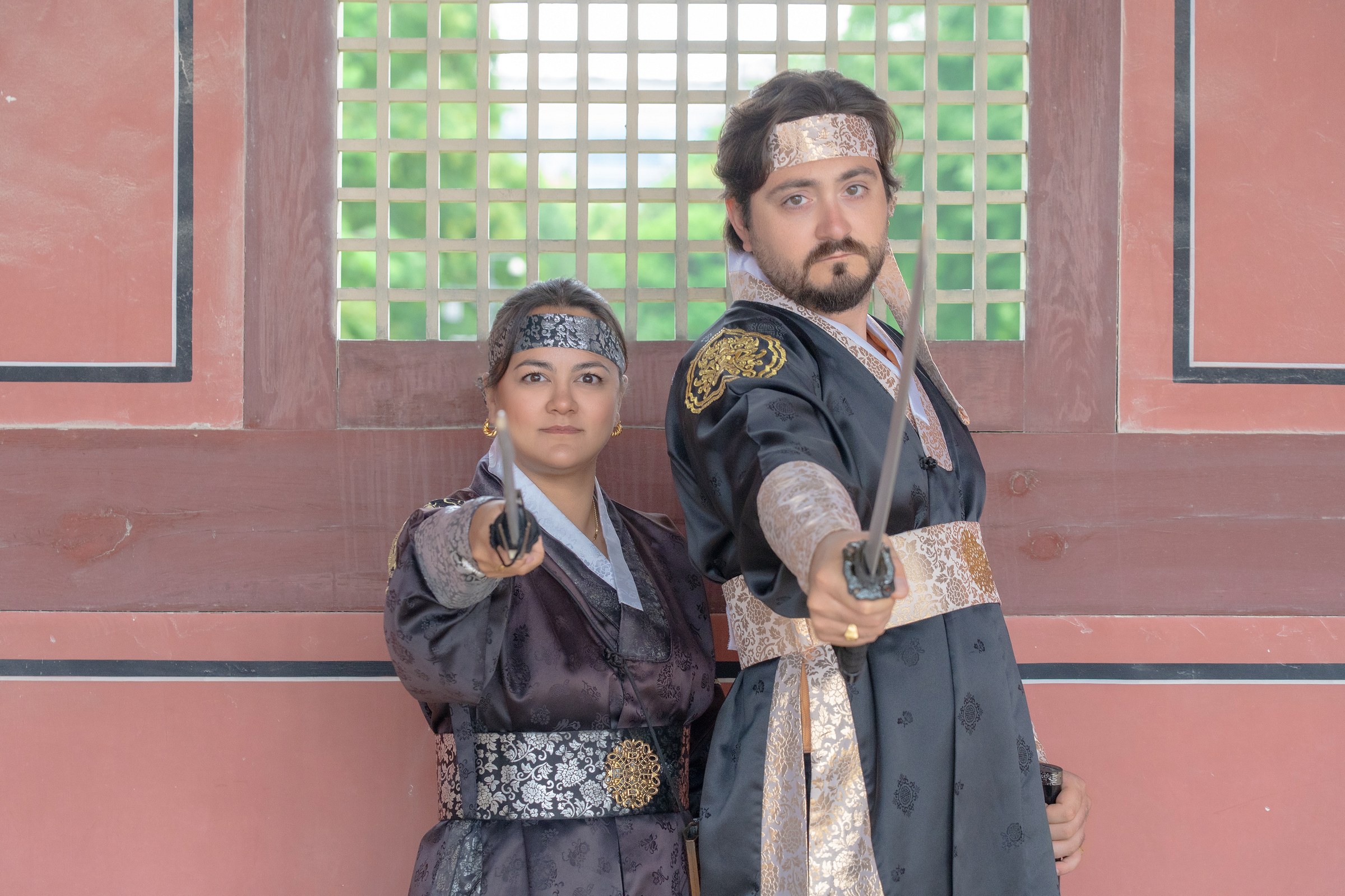 A couple in coordinated black hanbok posing in front of a red palace wall at Gyeongbokgung