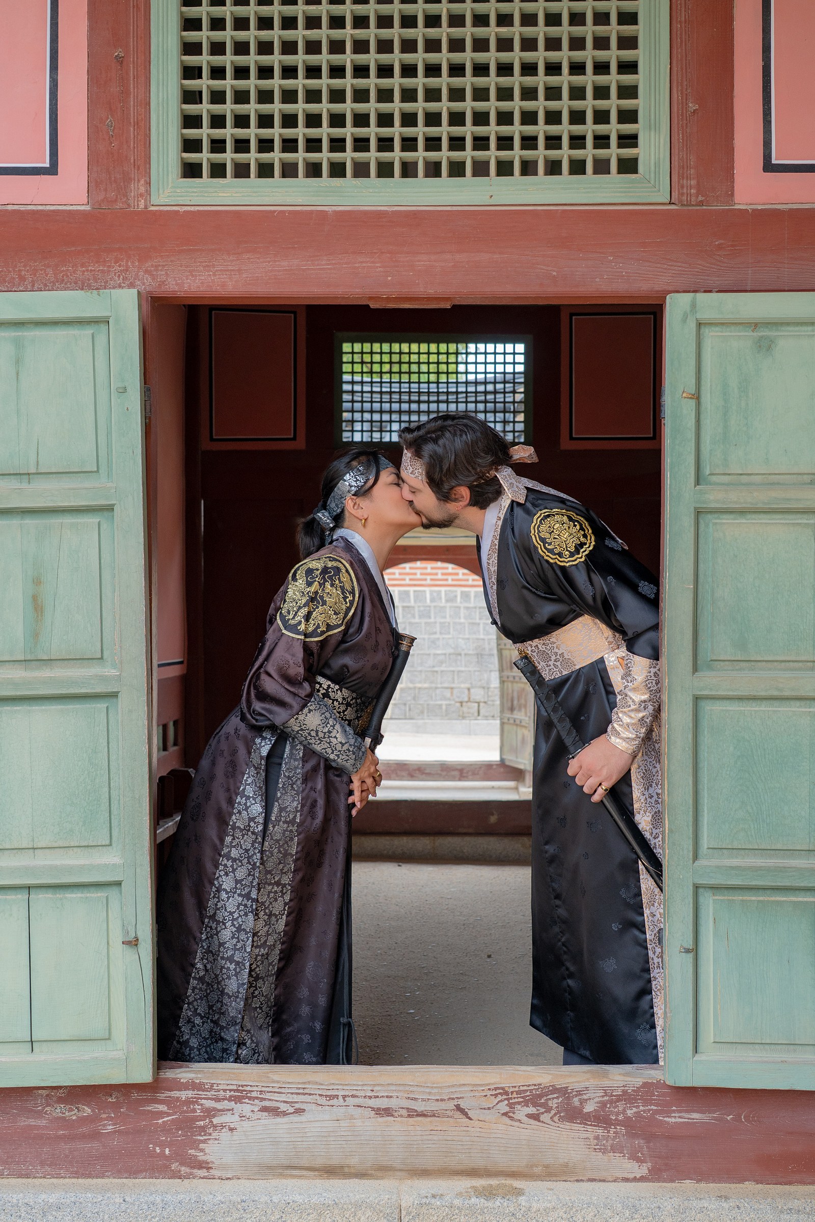 A couple in black hanbok sharing a kiss between open palace doors at Gyeongbokgung