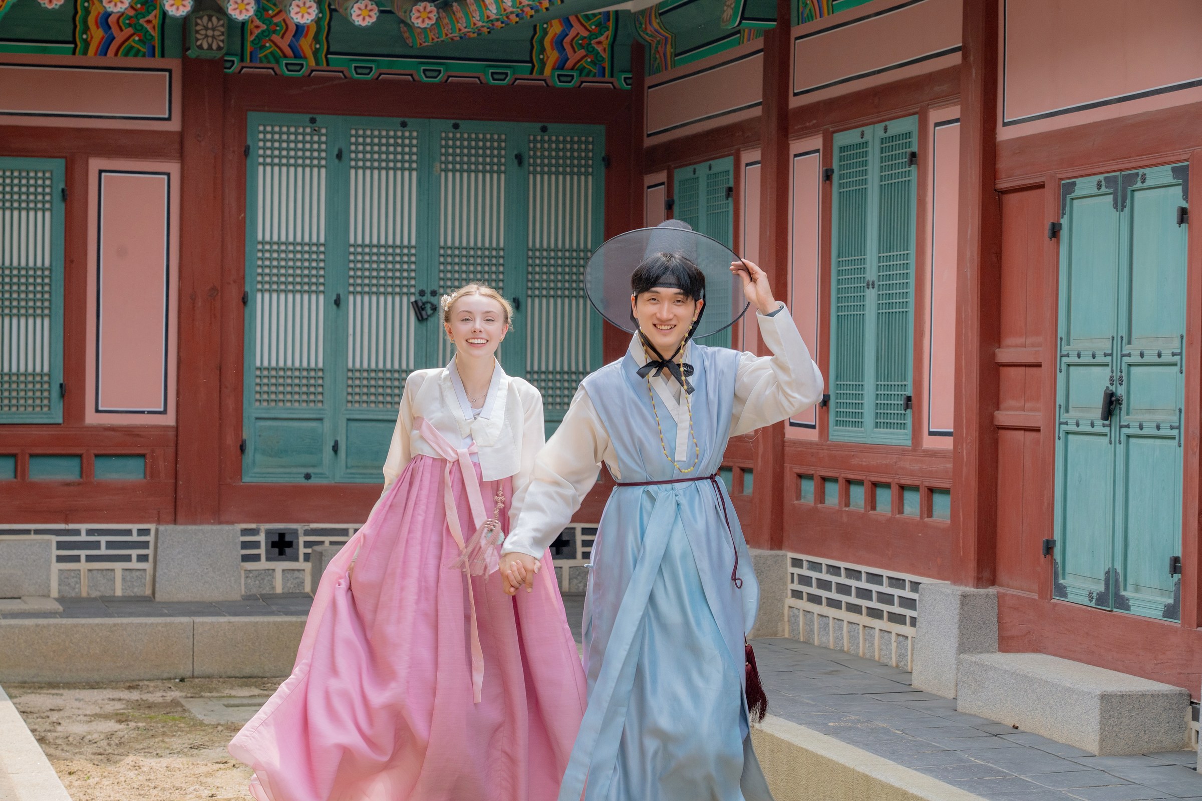 A smiling couple walking hand in hand through a colorful Gyeongbokgung courtyard
