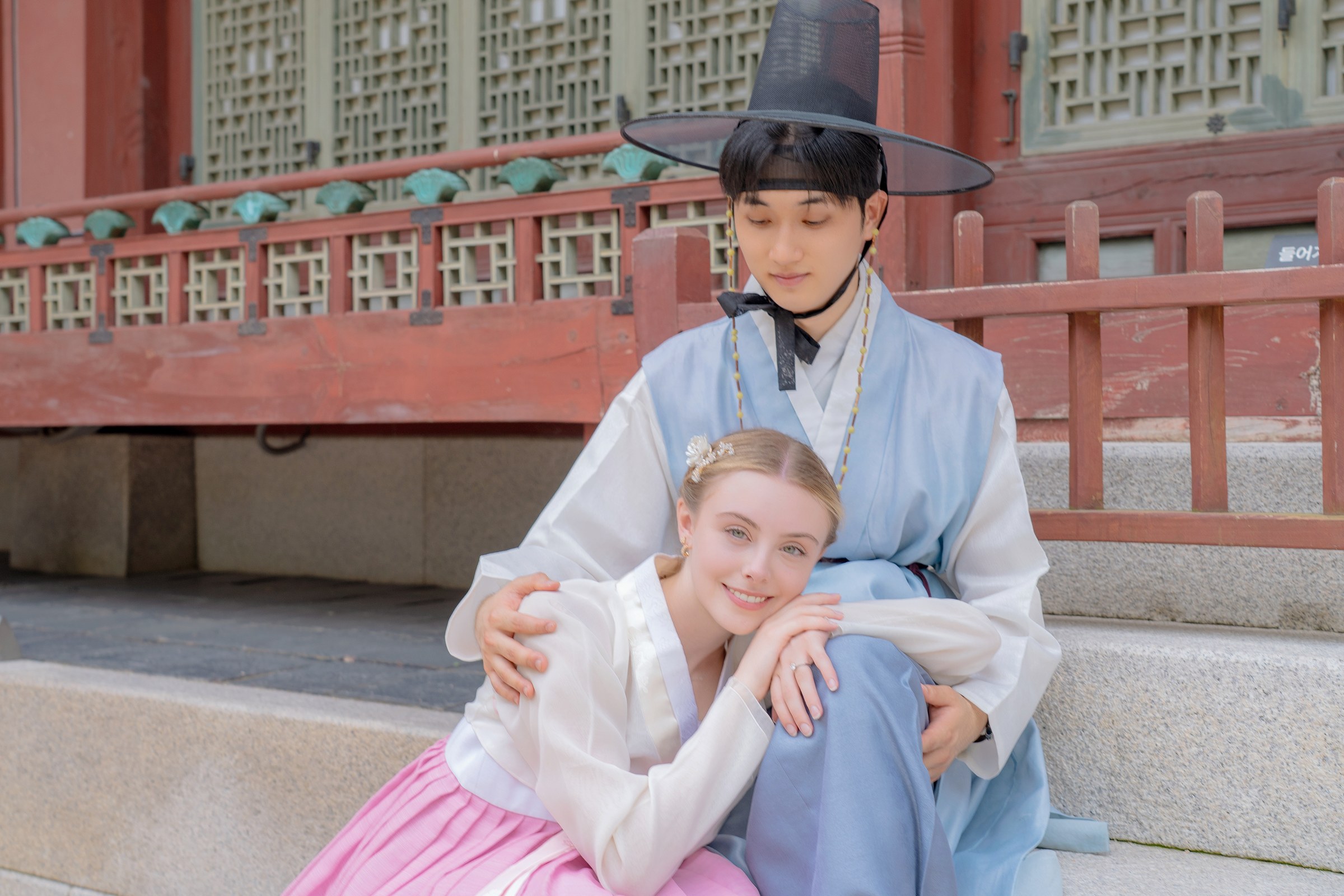 A relaxed seated portrait of a couple wearing pastel hanbok at Gyeongbokgung