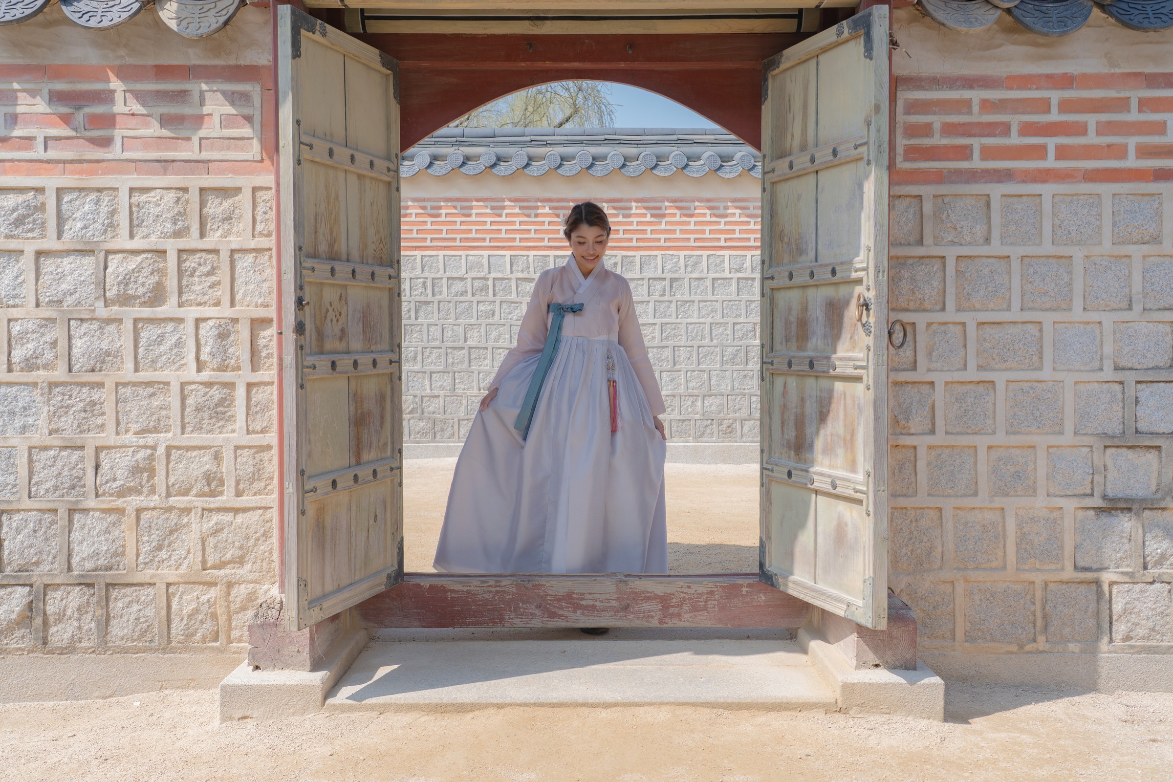A solo portrait in pale blue hanbok framed by an open palace doorway