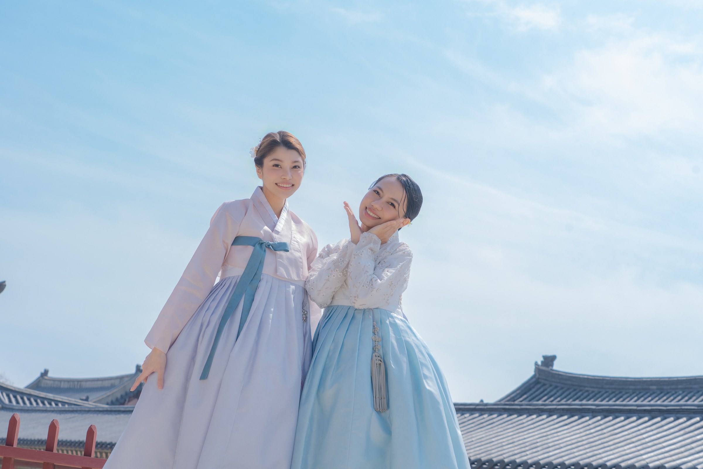A low-angle portrait of two friends from the Philippines in blue hanbok under a clear Seoul sky