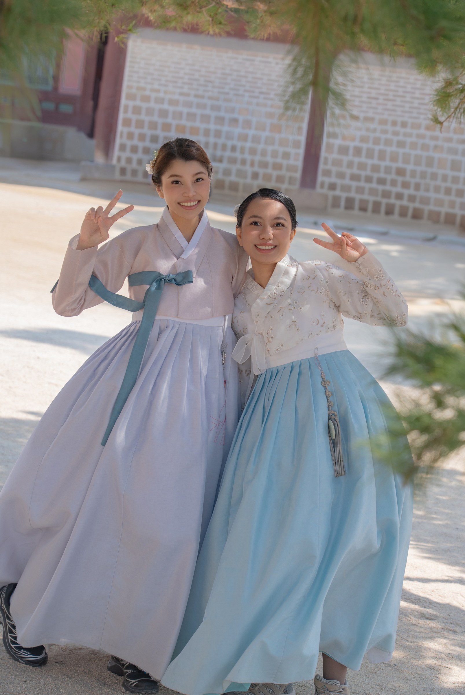 Two friends from the Philippines smiling and making peace signs in matching blue hanbok